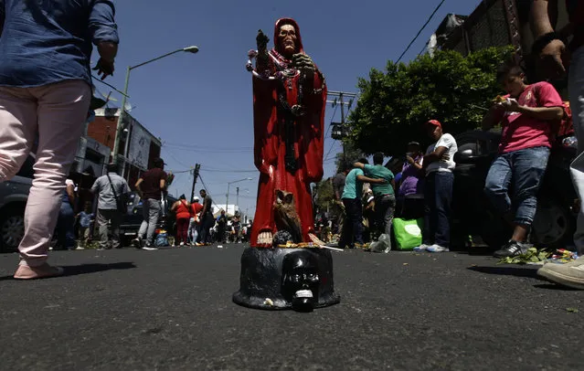 In this March 1, 2017 photo, a Death Saint or “Santa Muerte” statuette stands in the middle of the road, placed there by its owner who waits for people to offer it things like food, tobacco and alcohol, in Mexico City's Tepito neighborhood. According to popular belief, “Santa Muerte” is very powerful and is reputed to grant many favors. (Photo by Marco Ugarte/AP Photo)