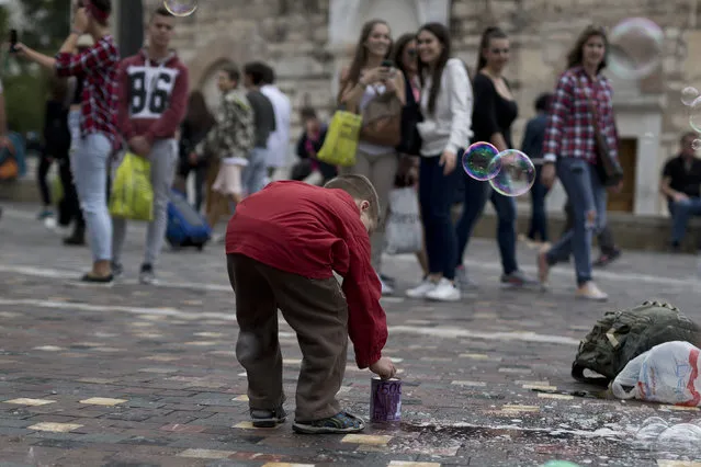 A boy puts coins in a tin, bearing the design of a 500-euro bank note, for a performer creating soap bubbles in Monastiraki Square, central Athens, on Wednesday, May 4, 2016. The European Central Bank will stop issuing 500 euro ($575) banknotes towards the end of 2018 on concerns it could facilitate illicit activities but outstanding bills will remain in use indefinitely, the ECB said in a statement on Wednesday. (Photo by Petros Giannakouris/AP Photo)