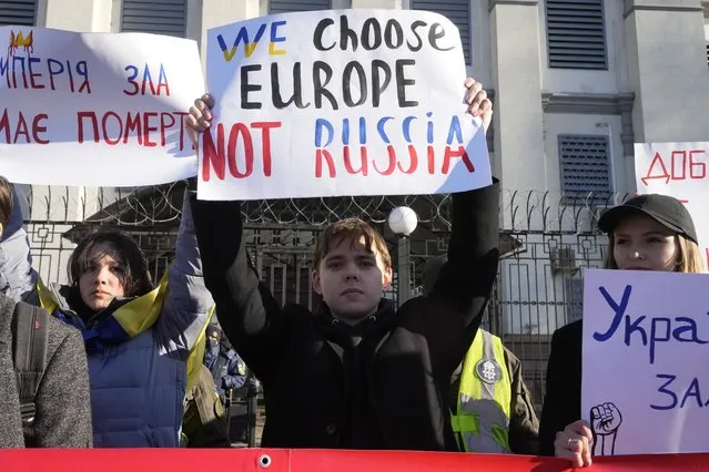 Protesters hold posters in front of the Russian Embassy in Kyiv, Ukraine, Tuesday, February 22, 2022. Russia says that its recognition of independence for areas in eastern Ukraine extends to territory currently held by Ukrainian forces. That announcement Tuesday further raises the stakes amid Western fears that a full-fledged invasion of Ukraine is imminent. (Photo by Efrem Lukatsky/AP Photo)