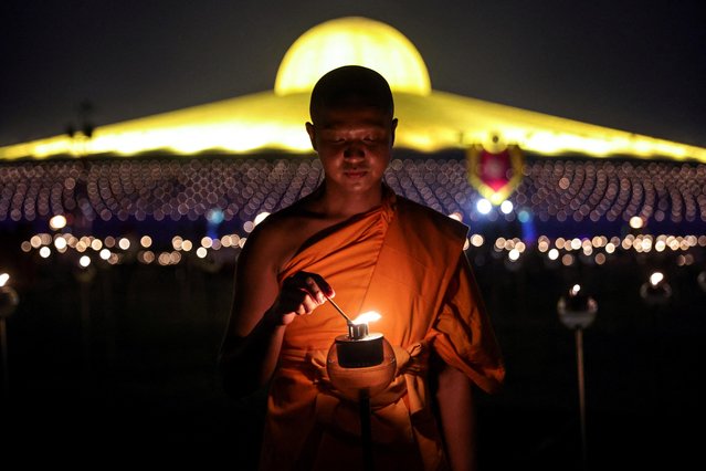A Buddhist monk lights up a candle light at the Wat Phra Dhammakaya temple during a ceremony commemorating Makha Bucha Day in Pathum Thani province outside Bangkok, Thailand on March 6, 2023. (Photo by Athit Perawongmetha/Reuters)