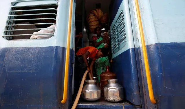 Siddharth's mother Jyoti Dhage holds her four month old daughter Akansha as she watches her neighbour Gaurav Ganesh, 13, as he helps fill the containers with water at Aurangabad railway station, India, July 18, 2019. “I'm careful, but sometimes pitchers fall off the door in the melee and our work is wasted”, she said. “I can't leave my daughter at home alone so I have to take her along”. (Photo by Francis Mascarenhas/Reuters)