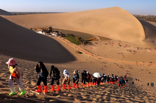 Tourists wearing shoe protectors climb up a dune with the overlook view of Crescent Spring at Mingsha Mountain, during an organised media tour to Dunhuang, in Gansu province, China on October 15, 2024. (Photo by Tingshu Wang/Reuters)