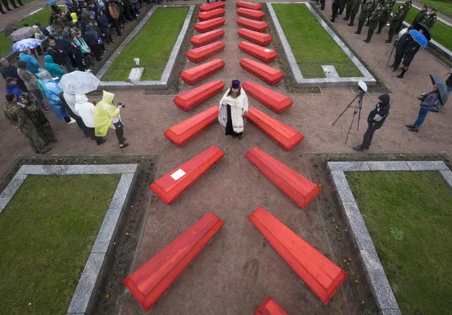 An Orthodox priest conducts a burial ceremony of Soviet soldiers killed during World War II who were discovered by members of volunteer search teams digging for remains on a former battlefield, in a memorial cemetery at Nevsky Pyatachok near Kirovsk, Russia, Tuesday, September 19, 2017. As many as 200,000 Soviet soldiers were killed here between September 1941 and May 1943 in fighting to break the Nazi siege of the city, which was then called Leningrad. The remains of 228 were buried Tuesday. (Photo by Dmitri Lovetsky/AP Photo)