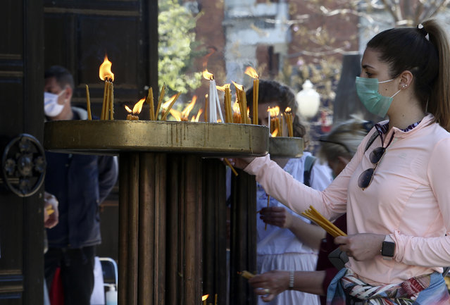 In this Thursday, April 16, 2020, photo, a young woman wearing a face mask to protect herself from the coronavirus lights candles in front of St. Clement Christian Orthodox Church in Skopje, North Macedonia. For Orthodox Christians, this is normally a time of reflection, communal mourning and then joyful release, of centuries-old ceremonies steeped in symbolism and tradition. But this year, Easter – by far the most significant religious holiday for the world's roughly 300 million Orthodox – has essentially been cancelled.  (Photo by Boris Grdanoski/AP Photo)