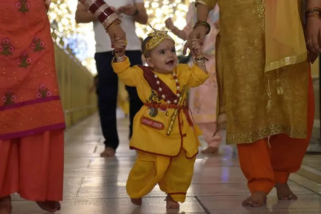 A child dressed as Hindu god Krishna walks along with his parents at the Durgiana Temple on the eve of 'Janmashtami' festival, marking the birth of Lord Krishna, in Amritsar on August 18, 2022. (Photo by Narinder Nanu/AFP Photo)