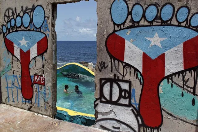 This August 25, 2017 photo shows a couple swimming, framed by a concrete wall blanketed with graffiti, in the seaside slum La Perla, in San Juan, Puerto Rico. La Perla is suddenly a popular tourism spot thanks in part to this year's hit song “Despacito”, whose video became the most-watched in YouTube history. (Photo by Ricardo Arduengo/AP Photo)