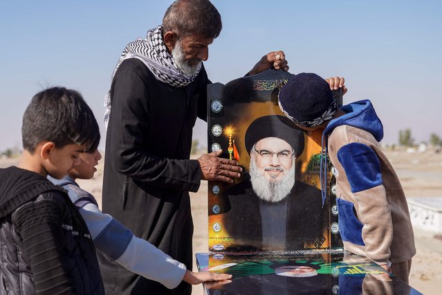 A man and children pray by a symbolic grave for slain Lebanon's Hezbollah leader Hasan Nasrallah in Iraq's Shiite holy city of Najaf, on November 15, 2024. Nasrallah was killed in an Israeli air strike on Beirut's southern suburbs on September 27, 2024, amid the ongoing war between Israel and Hezbollah. (Photo by Qassem Al-Kaabi/AFP Photo)