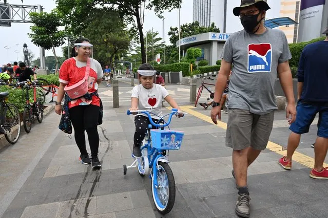 People wearing face shields walk along a street in Jakarta on June 7, 2020, as the capital city loosens a partial lockdown despite COVID-19 coronavirus cases mounting in the world’s biggest Muslim majority nation. (Photo by Adek Berry/AFP Photo)
