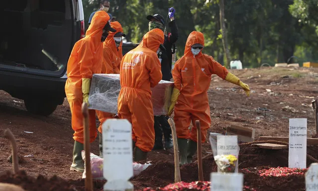 Workers in protective suits carry the coffin of a suspected victim of COVID-19 during a burial at Pondok Ranggon cemetery in Jakarta, Indonesia, Friday, June 12, 2020. (Photo by Achmad Ibrahim/AP Photo)