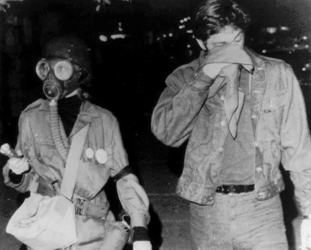 In this August 27, 1968, file photo, a woman wears a gas mask as she walks with a companion holding a cloth to his eyes after they were sprayed with tear gas during protests on Chicago's North Side. The Associated Press found that there is no government oversight of the manufacture and use of tear gas. Instead, the industry is left to regulate itself. (Photo by AP Photo/File)