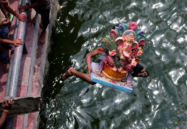 A devotee carrying an idol of the Hindu god Ganesh, the deity of prosperity, jumps into the Sabarmati river to immerse the idol on the last day of the ten-day-long Ganesh Chaturthi festival in Ahmedabad, India, September 15, 2016. (Photo by Amit Dave/Reuters)