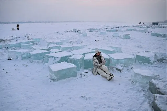 A woman poses beside blocks of cut ice on the frozen Songhua river in Harbin, in China's northeastern Heilongjiang province, on January 6, 2023. (Photo by Hector Retamal/AFP Photo)