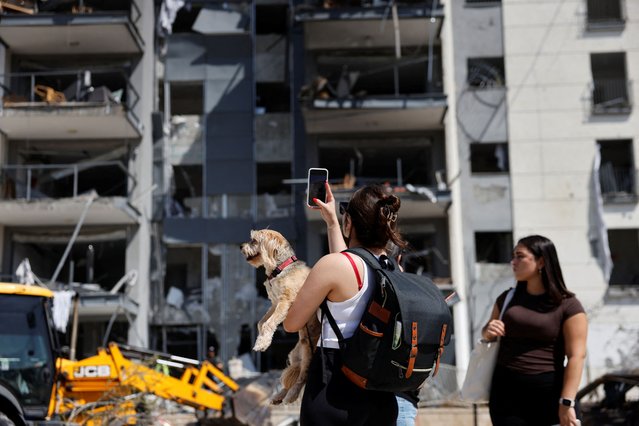 A woman holding a dog takes a photo of a damaged residential building at an impact site following Iran's missile strike on Israel, in Be'er Sheva, Israel, on June 20, 2025. (Photo by Amir Cohen/Reuters)
