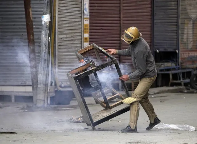 An Indian policeman removes a damaged table after it was set on fire by the supporters of Jammu Kashmir Liberation Front (JKLF), a Kashmiri separatist party, during a protest in Srinagar October 20, 2015 against the detention of its chief, Mohammad Yasin Malik. Malik was detained in Anantnag district as he was planning to sit on a hunger strike to protest the killing of a Kashmir trucker over rumours he was involved in cow slaughter in the Hindu dominated Jammu region. (Photo by Danish Ismail/Reuters)