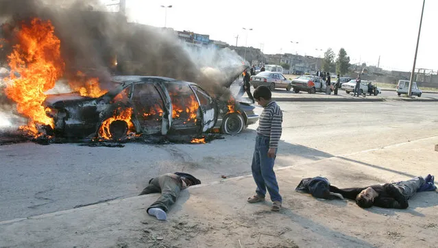 An Iraqi boy looks at the bodies of four men laying next to their burning car after they were attacked by gunmen in the northern Iraq city of Mosul, on December 17, 2004. Insurgents attacked a car carrying at least three Westerners, killing them and their Iraqi driver, and chopping off the head of one victim, local witnesses said. (Photo by Namir Noor-Eldeen/Reuters/The Atlantic)