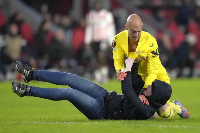 A PSV supporter, on the ground, attacks Sevilla's goalkeeper Marko Dmitrovic during the Europa League playoff second leg soccer match between PSV and Sevilla at the Philips stadium in Eindhoven, Netherlands, Thursday, February 23, 2023. Sevilla won 3-2 on aggregate. (Photo by Peter Dejong/AP Photo)