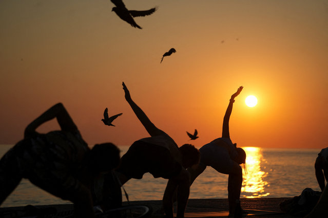A group of people practice yoga during sunrise at the beach, during the second heat wave of the summer in Barcelona, Spain on August 5, 2025. (Photo by Bruna Casas/Reuters)