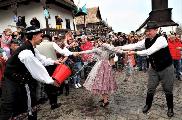 A woman wearing traditional clothes reacts as men throw water at her during a traditional Easter celebration in Holloko, Hungary on April 10, 2023. (Photo by Bernadett Szabo/Reuters)
