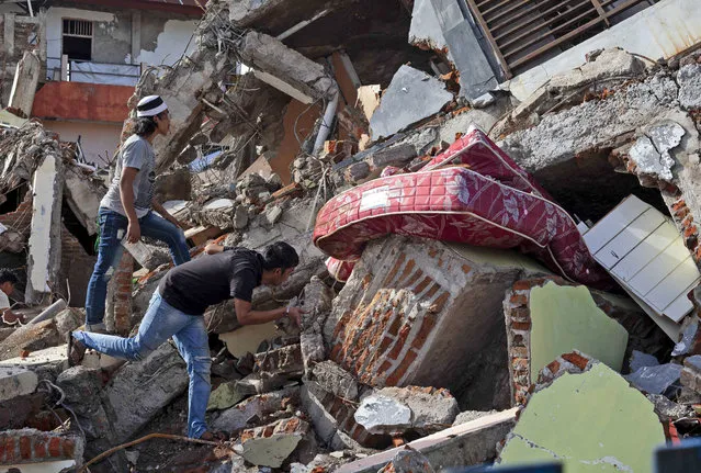 Residents inspect a building collapsed in Friday's earthquake in Mamuju, West Sulawesi, Indonesia, Monday, January 18, 2021. Aid was reaching the thousands of people left homeless and struggling after an earthquake that killed a number of people in the province where rescuers intensified their work Monday to find those buried in the rubble. (Photo by Yusuf Wahil/AP Photo)