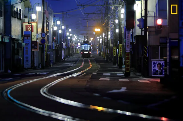 “First Train in the Street”. “The Enoshima railway runs on a street in a shopping district in Japan. There are people and cars during the day. Few were out in the early morning, when the first train ran slowly and the rails were wet with rain and appeared to glow”. (Photo by Hideyuki Katagiri/National Geographic Travel Photographer of the Year Contest)