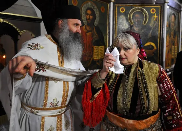 A woman stands next to a priest during an Epiphany day celebration in Bitushe village, about 150km (93 miles) west from the capital Skopje, January 19, 2015. Bitushe practises a different Epiphany tradition. Instead of jumping into the water to retrieve a cross thrown by a priest, the village's women carry homemade bread on their heads while dressed in folk costumes to mark the welfare and health of their families. (Photo by Ognen Teolovski/Reuters)