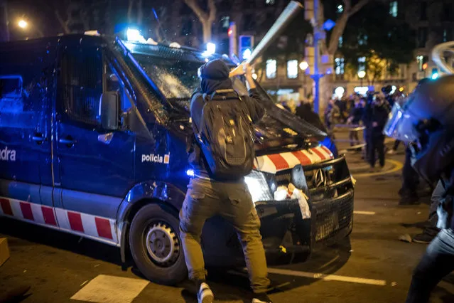 A demonstrator hits a police van with a bat during clashes following a protest condemning the arrest of rap singer Pablo Hasél in Barcelona, Spain, Wednesday, February 17, 2021. Police fired rubber bullets and baton-charged protesters as clashes erupted for a second night in a row Wednesday at demonstrations over the arrest of Spanish rap artist Pablo Hasél. Many protesters threw objects at police and used rubbish containers and overturned motorbikes to block streets in both Madrid and Barcelona. (Photo by Emilio Morenatti/AP Photo)