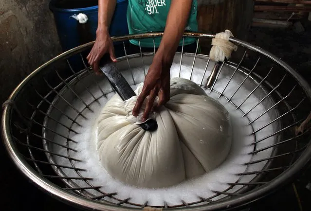 A worker filtrates hot boiled soybean porridge using a soft cloth in a traditional tofu factory in Depok, Indonesia, 21 January 2015. (Photo by Adi Weda/EPA)