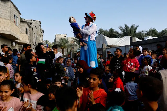 A Palestinian dressed in a clown costume entertains children, in Deir al-Balah, central Gaza Strip on May 15, 2023. (Photo by Ibraheem Abu Mustafa/Reuters)
