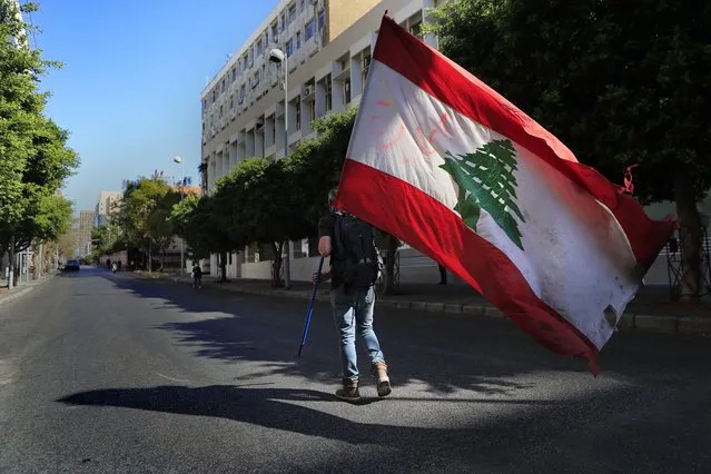 A protester holds a Lebanese flag, as he walks on a blocked main road that leads to the Central Bank during a protest against the increase in prices of consumer goods and the crash of the local currency, in Beirut, Lebanon, Tuesday, March 16, 2021. Scattered protests broke out on Tuesday in different parts of the country after the Lebanese pound hit a new record low against the dollar on the black market. (Photo by Hussein Malla/AP Photo)