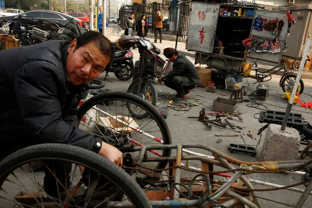 A man repairs a three-wheeled vehicle (foreground) typically used by garbage collectors at a pop-up repair shop on a pavement in Beijing, China, November 3, 2016. (Photo by Thomas Peter/Reuters)
