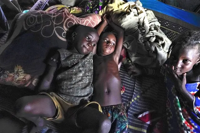 Children rest in a hut on the side of the road crowded with some 140 people in Niamey, Niger, Monday, July 31, 2023. In the capital of Niger, many people live in makeshift shelters tied together with slats of wood, sheets and plastic tarps because they can't pay rent, and they scramble daily to make enough money to feed their children. (Photo by Sam Mednick/AP Photo)