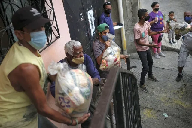 Residents help to unload bags of basic food staples, such as pasta, sugar, flour and kitchen oil, provided by a government food assistance program, in the Santa Rosalia neighborhood of Caracas, Venezuela, Saturday, April 10, 2021. The program known as Local Committees of Supply and Production, CLAP, provides subsidized food for vulnerable families, especially now in the midst of a quarantine to stop the COVID-19 pandemic that has left many without income. (Photo by Matias Delacroix/AP Photo)