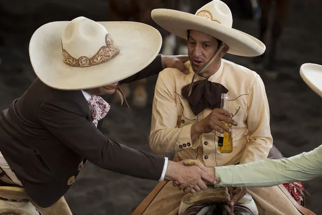 In this February 28, 2015 photo, charros drink and greet friends as they sit on horseback on the sidelines of a  charreada in Mexico City. Although winning is always an honor, said Manuel Basurto Rojas, president of the National Charros Association, the main importance of the infrequent national competitions is really “social harmony”. “It's primarily a chance to spend time with all the brotherhood of charreria from the entire Mexican republic”. (Photo by Rebecca Blackwell/AP Photo)