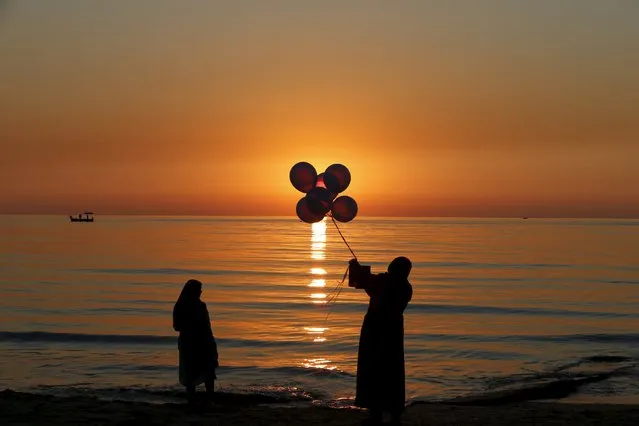 A woman holds balloons as she takes photographs of her friend during sunset on a warm day at Beirut beach, Lebanon, January 13, 2016. (Photo by Jamal Saidi/Reuters)