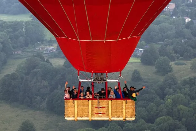 People wave from a hot air balloon as it flies during a mass launch at the annual Bristol International Balloon Fiesta, in Bristol, Britain on August 11, 2023. (Photo by Toby Melville/Reuters)