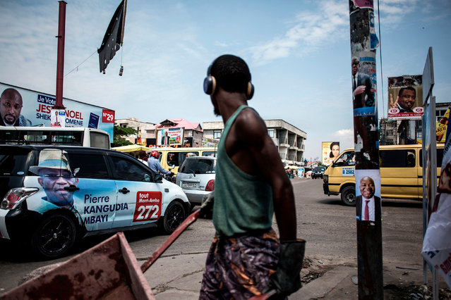 A construction worker pushes a wheelbarrow past a campaign car and posters at a busy intersection in the district of Lingwala in Kinshasa on December 18, 2018. Democratic Republic of Congo goes to the polls on December 23, 2018 in elections which could see the country emerge from 17 years of conflict-ridden rule under controversial President Joseph Kabila. (Photo by John Wessels/AFP Photo)