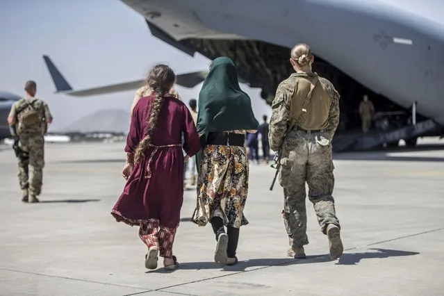 In this image provided by the U.S. Marine Corps, a Marine with the 24th Marine Expeditionary Unit walks with a family during ongoing evacuations at Hamid Karzai International Airport, Kabul, Afghanistan, Tuesday, August 24, 2021. (Photo by Sgt. Samuel Ruiz/U.S. Marine Corps via AP Photo)