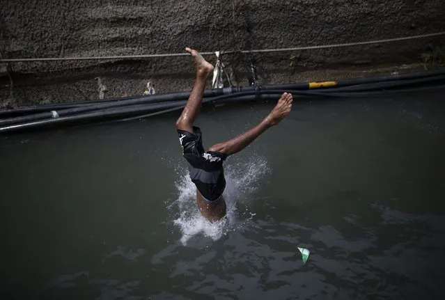 A boy dives into a drainage ditch which channels water from an abandoned highway tunnel in Caracas, Venezuela, Thursday, July 15, 2021. People use the drainage ditch to do laundry, take a shower, collect water to take their houses and also as a pool for children to enjoy. (Photo by Ariana Cubillos/AP Photo)