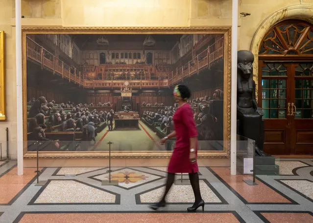 A passerby views the painting Devolved Parliament, by the graffiti artist Banksy, which is going on show at Bristol Museum in England on March 28, 2019. (Photo by Steve Parsons/PA Wire Press Association)