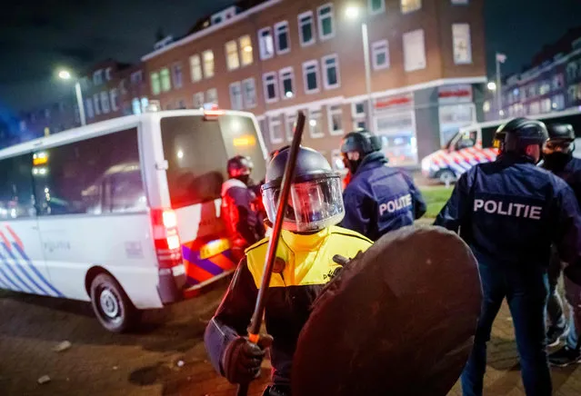 A policeman with helmet and shield holds a baton as he stands next to a policevan on Beijerlandselaan in Rotterdam, on January 25, 2021. The Netherlands was hit by a second wave of riots on January 25 evening after protesters again went on the rampage in several cities following the introduction of a coronavirus curfew over the weekend. Riot police clashed with groups of protesters in the port city of Rotterdam, where they used a water canon. (Photo by Marco de Swart/ANP/AFP Photo)