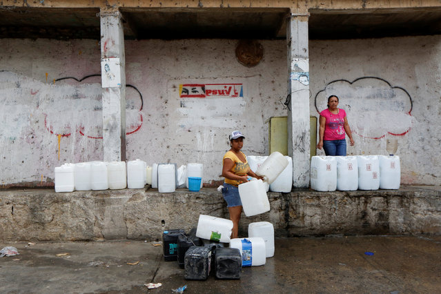 Alexandra Evaristo (C) and Balbina Ortega pose for a picture next to their plastic containers used to carry water, near a well on a street, close to a neighbourhood called “The Tank” at the slum of Petare in Caracas, Venezuela, April 3, 2016. (Photo by Carlos Garcia Rawlins/Reuters)