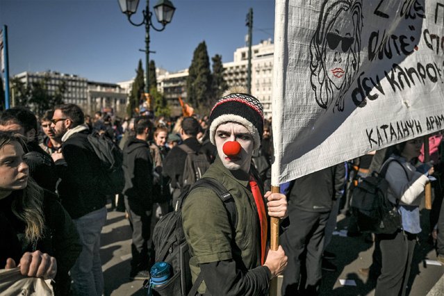 An artist wearing a clown nose holds a banner during a demonstration in front of the Greek parliament in Athens, on February 2, 2023. Around one thousand and eight hundred artists and art students, according to police, demonstrated in Athens on February 2, 2023, against a draft law, which puts their degrees on the same footing as bachelor's degrees in terms of pay and professional qualifications. (Photo by Aris Messinis/AFP Photo)