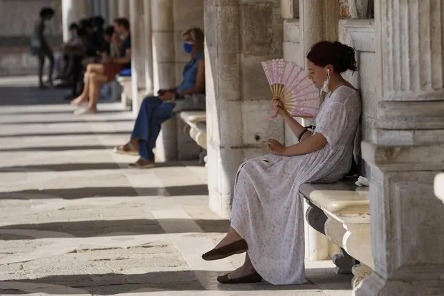 Tourists relax in the shade in St. Mark's square, in Venice, Italy, Thursday, June 17, 2021. After a 15-month pause in mass international travel, Venetians are contemplating how to welcome visitors back to the picture-postcard canals and Byzantine backdrops without suffering the indignities of crowds clogging its narrow alleyways, day-trippers perched on stoops to imbibe a panino and hordes of selfie-takers straining for a spot on the Rialto Bridge or in front of St. Mark’s Basilica. (Photo by Luca Bruno/AP Photo)