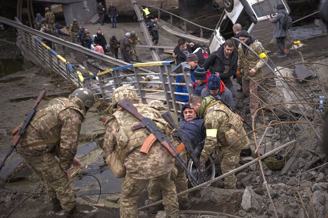 Ukrainian soldiers help a man on a wheelchair as people try to flee crossing the Irpin river in the outskirts of Kyiv, Ukraine, Saturday, March 5, 2022. (Photo by Emilio Morenatti/AP Photo)