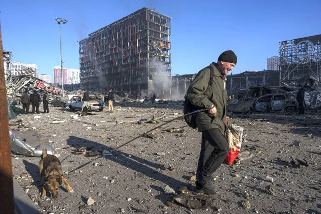A man walks with his dog amid the destruction caused after shelling of a shopping center, in Kyiv, Ukraine, Monday, March 21, 2022. (Photo by Rodrigo Abd/AP Photo)