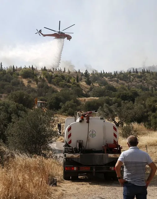 A helicopter drops water over flames on the mountain of Ymittos in Athens, Friday, July 17, 2015. (Photo by Petros Giannakouris/InTime News via AP Photo)