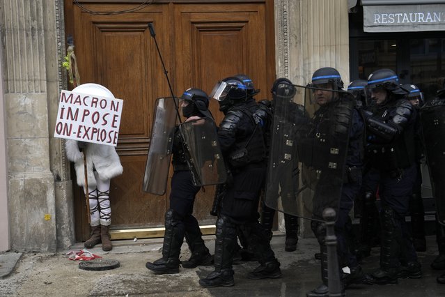 A protester hides behind a poster reading “Macron impose, we explode” during a demonstration, Thursday, April 13, 2023 in Paris. Protesters opposed to President Emmanuel Macron's unpopular plan to raise the retirement age in France marched Thursday in cities and towns around France in a final show of anger before a decision by the Constitutional Council on whether the measure meets constitutional standards. (Photo by Lewis Joly/AP Photo)