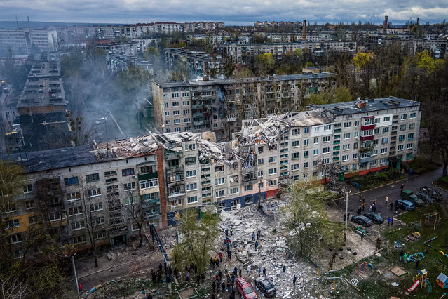 This aerial view shows rescuers on top of a partially destroyed residential building, after a shelling in Sloviansk, on April 14, 2023, amid Russia's military invasion on Ukraine. Russian shelling of a residential building in the eastern Ukrainian city of Sloviansk killed at least five people on April 14, the local governor said, warning that others could be buried in the rubble. (Photo by Ihor Tkachov/AFP Photo)