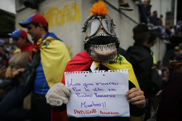 A masked man holds a sign that reads in Spanish “Those who die for life cannot be called dead!” and “Bolivarian National Guard (GNB), Bolivarian National Police (PNB) killers” marches with others to the site where protester Neomar Lander died in Caracas, Venezuela, Thursday, June 8, 2017. Lander, 17, is one of the latest victims of Venezuela's unrest. He died during anti-government protests on Wednesday. (Photo by Ariana Cubillos/AP Photo)