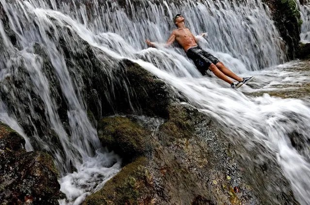 A man enjoys a waterfall at the lake in the central Bosnian town of Jajce, Bosnia and Herzegovina, August 5, 2015. (Photo by Dado Ruvic/Reuters)